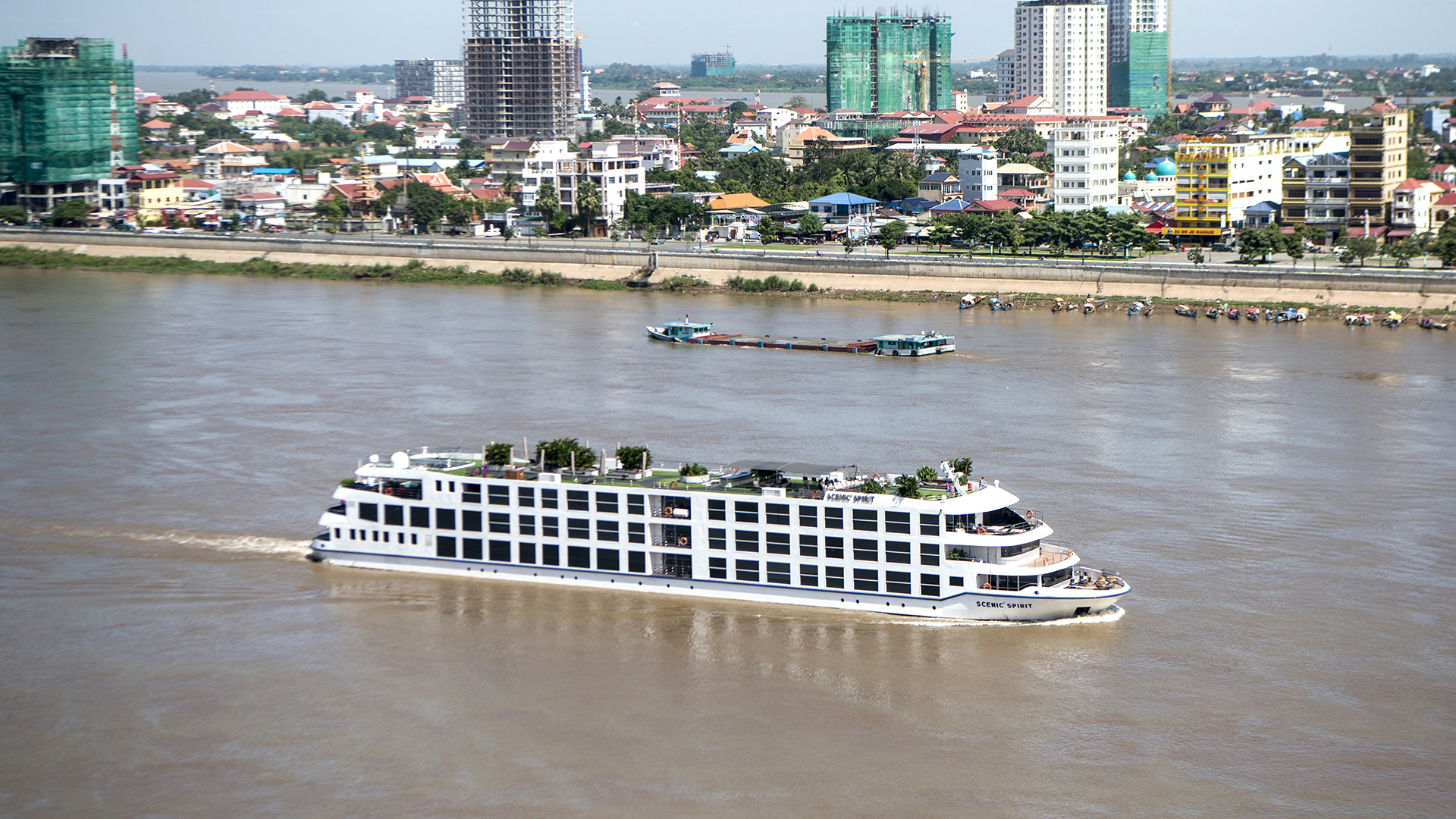 Three-deck river cruise ship passing a modern riverside city