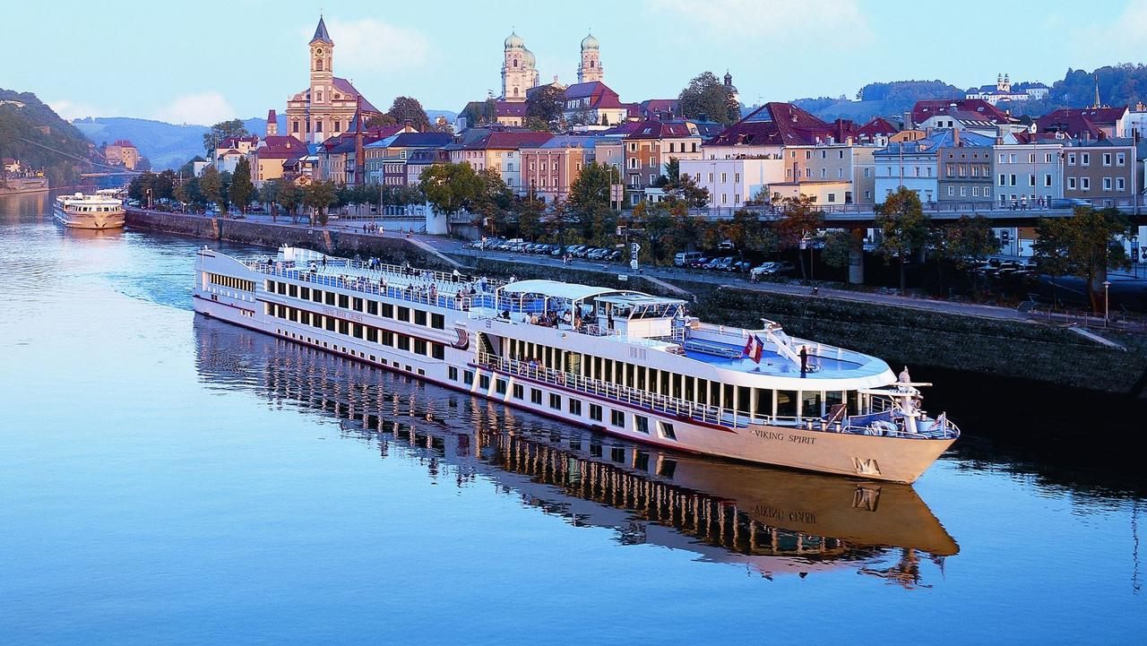 River cruise ship moored on a calm river in front of an old town with baroque towers